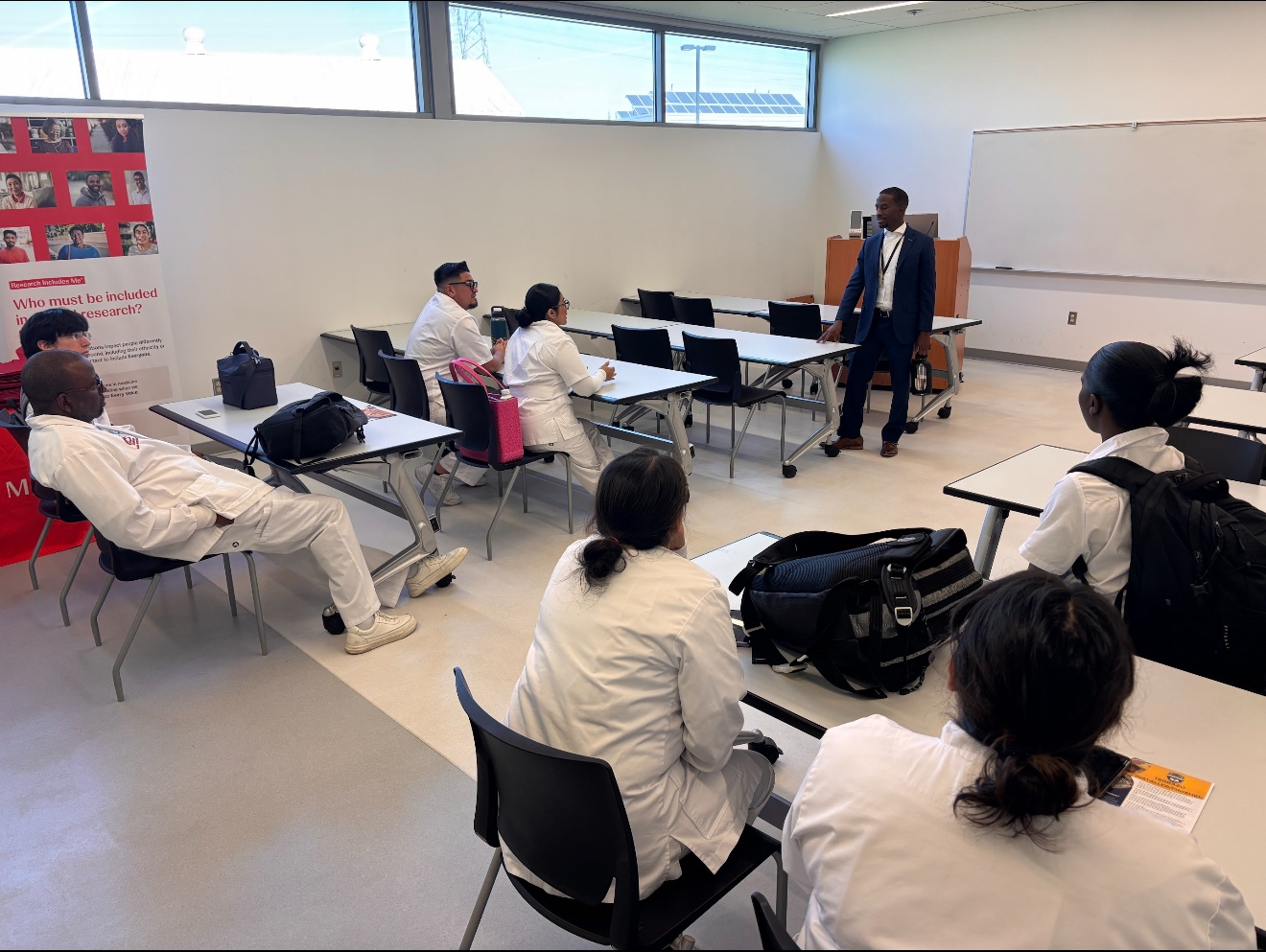 A presenter speaks with attendees seated in a classroom.