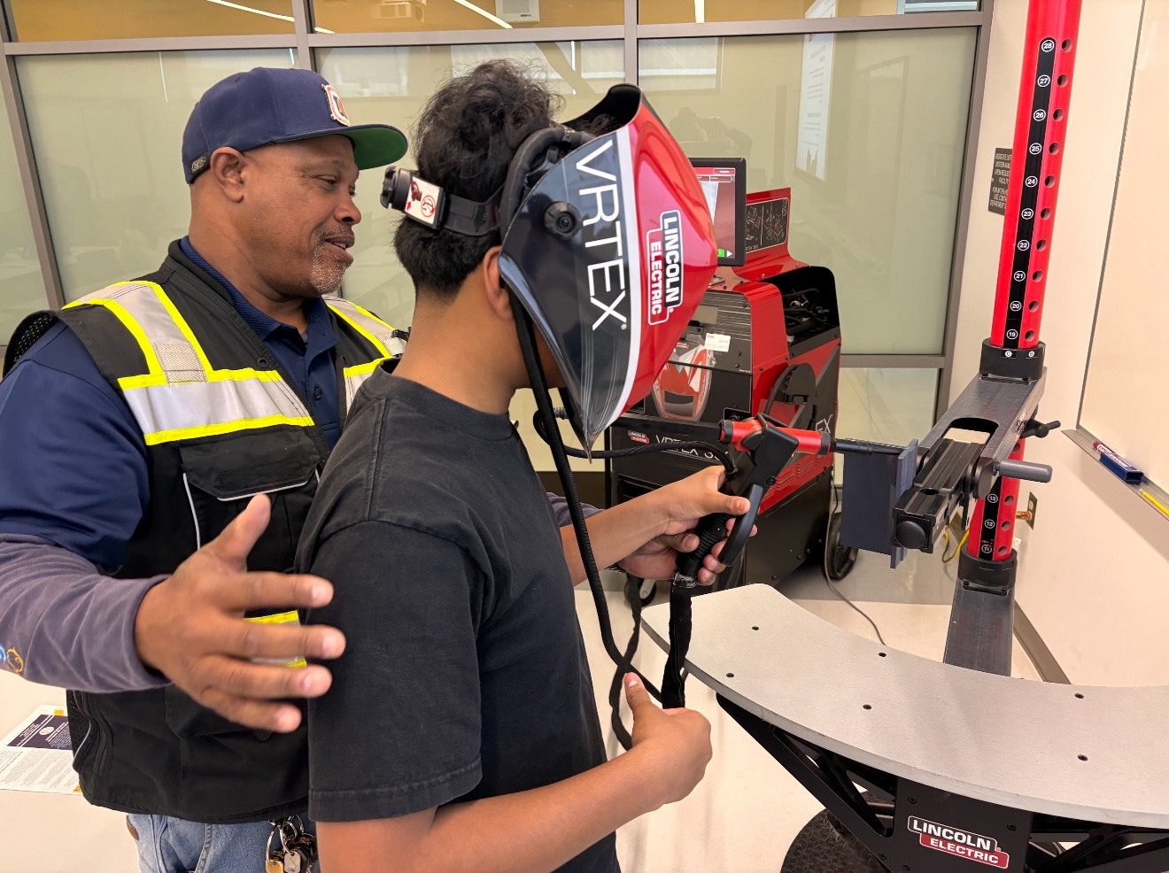 A participant uses a virtual welding simulator with guidance from an instructor.